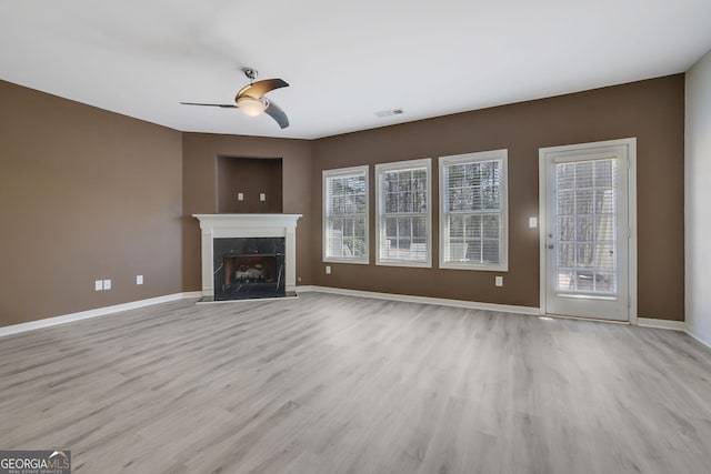 unfurnished living room featuring ceiling fan, a premium fireplace, a healthy amount of sunlight, and light wood-type flooring