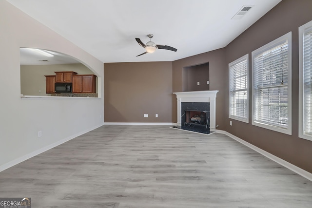 unfurnished living room featuring ceiling fan, a premium fireplace, and light wood-type flooring