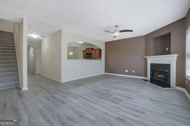 unfurnished living room with a fireplace, ceiling fan, and light wood-type flooring