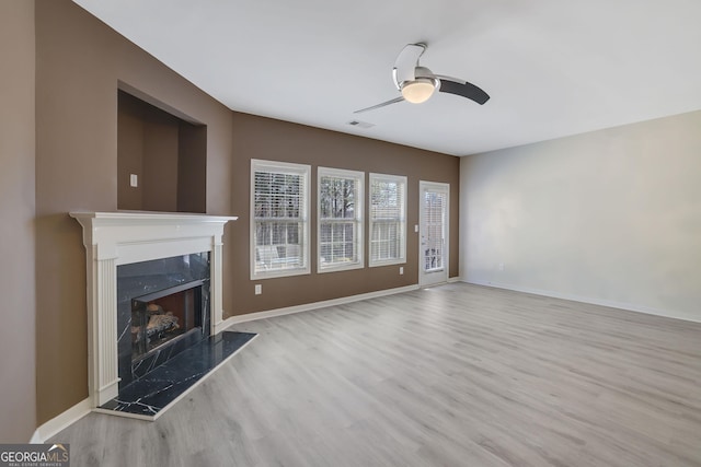 unfurnished living room featuring ceiling fan, light hardwood / wood-style flooring, and a premium fireplace