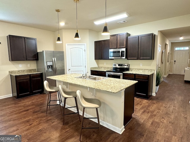 kitchen with dark wood-type flooring, a kitchen bar, dark brown cabinets, a center island with sink, and stainless steel appliances