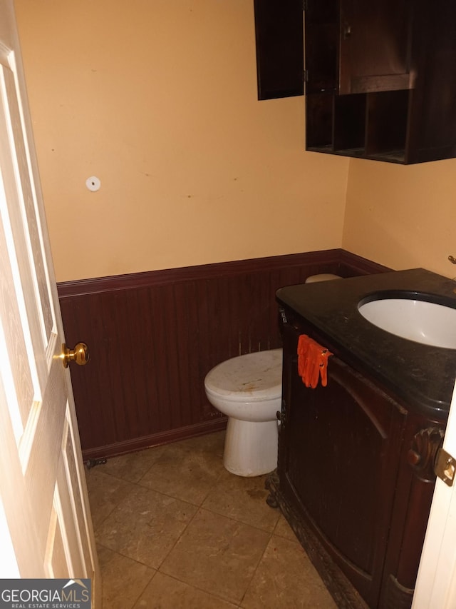 bathroom with wooden walls, vanity, toilet, and tile patterned floors