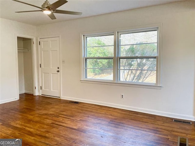 unfurnished bedroom featuring multiple windows, dark wood-type flooring, and ceiling fan