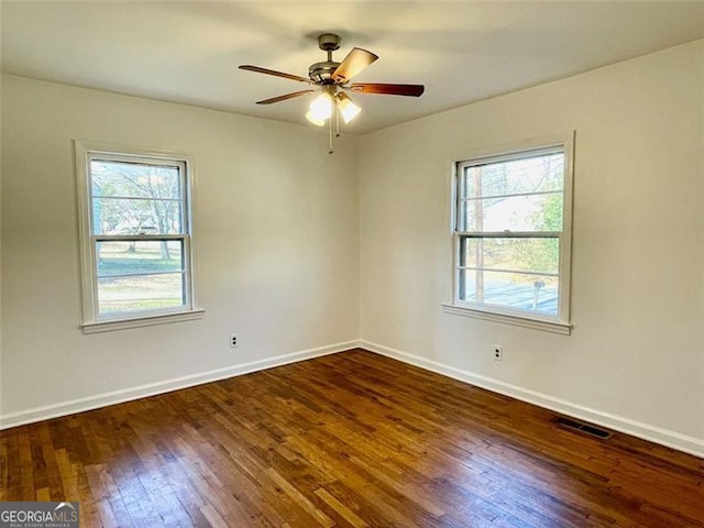 empty room with a wealth of natural light, dark hardwood / wood-style floors, and ceiling fan