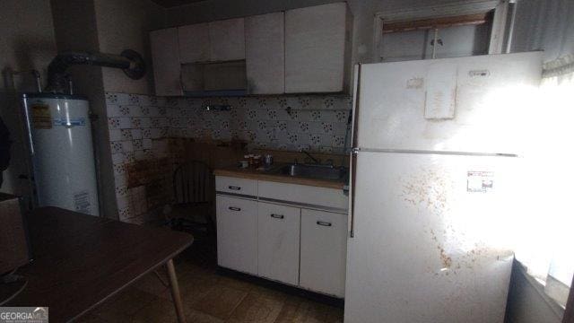 kitchen featuring gas water heater, white cabinetry, sink, white refrigerator, and hardwood / wood-style flooring