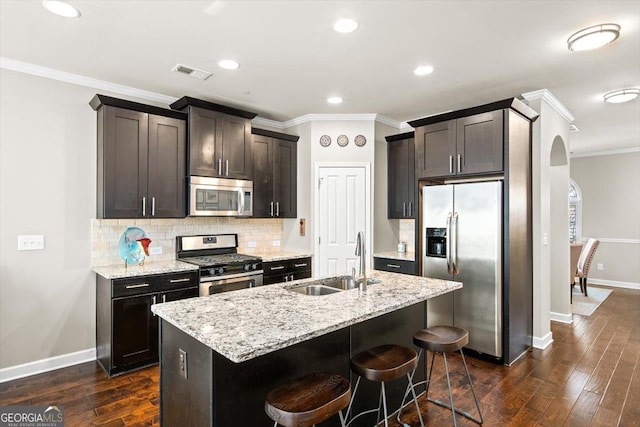 kitchen with a kitchen island with sink, sink, stainless steel appliances, and a kitchen bar