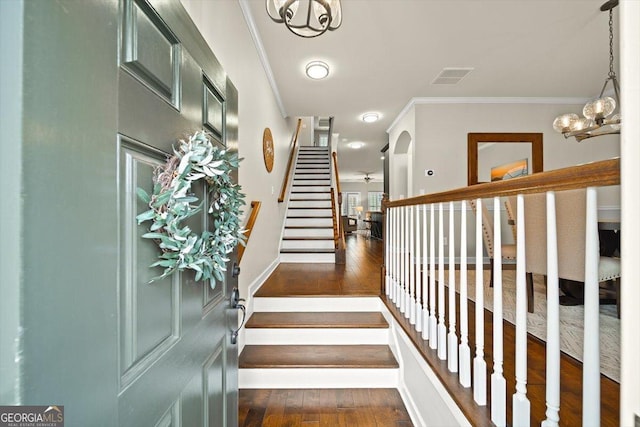 staircase featuring hardwood / wood-style floors, crown molding, and a chandelier