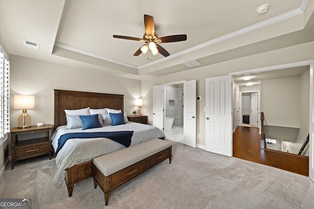 bedroom with crown molding, ensuite bath, ceiling fan, a tray ceiling, and light colored carpet