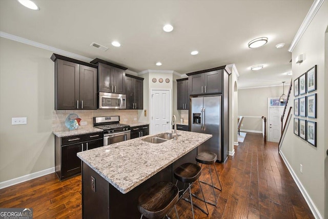 kitchen featuring sink, a breakfast bar area, light stone counters, appliances with stainless steel finishes, and an island with sink