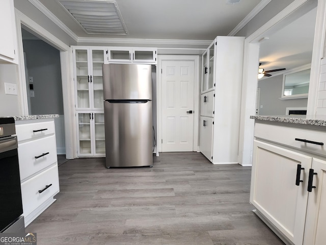 kitchen with stainless steel fridge, white cabinetry, light stone countertops, ornamental molding, and light wood-type flooring