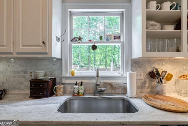 kitchen featuring light stone counters, sink, tasteful backsplash, and white cabinets