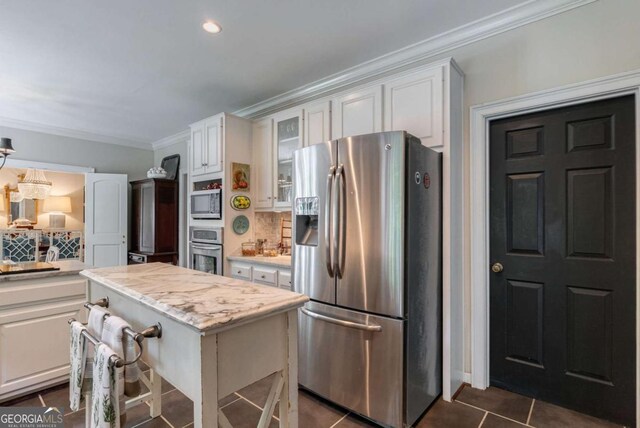 kitchen with a kitchen island, white cabinetry, dark tile patterned flooring, stainless steel appliances, and crown molding