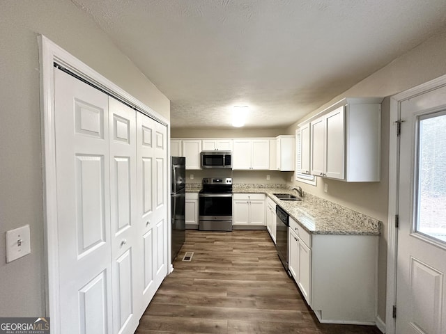 kitchen featuring appliances with stainless steel finishes, white cabinetry, sink, light stone countertops, and dark wood-type flooring