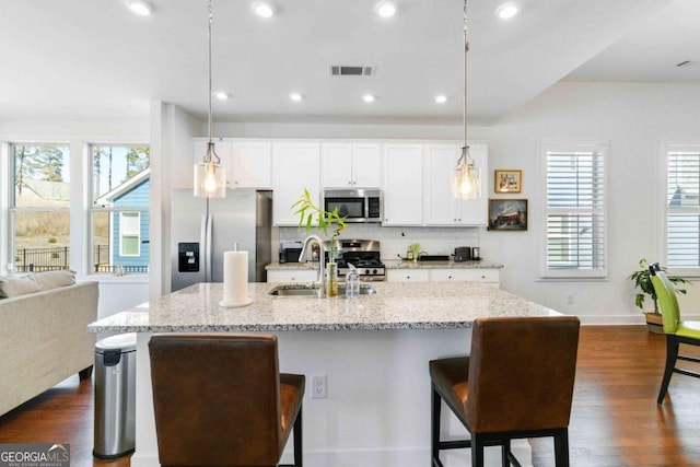 kitchen featuring pendant lighting, an island with sink, sink, light stone counters, and stainless steel appliances