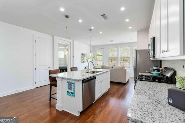 kitchen with sink, hanging light fixtures, a center island with sink, stainless steel appliances, and white cabinets