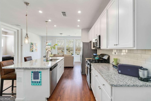 kitchen featuring pendant lighting, white cabinetry, an island with sink, sink, and stainless steel appliances