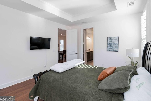 bedroom featuring dark hardwood / wood-style floors, ornamental molding, a raised ceiling, and ensuite bathroom