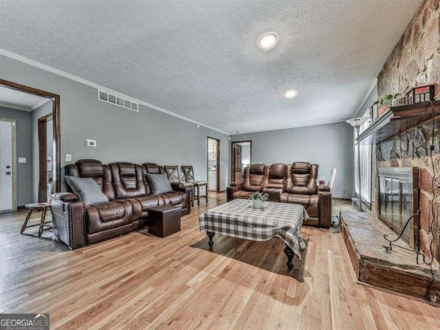 living room with ornamental molding, a fireplace, a textured ceiling, and light wood-type flooring