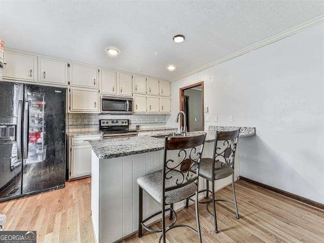 kitchen with appliances with stainless steel finishes, decorative backsplash, light stone counters, and light hardwood / wood-style flooring