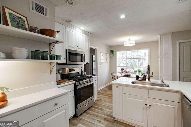 kitchen featuring sink, white cabinetry, a textured ceiling, stainless steel appliances, and light hardwood / wood-style floors