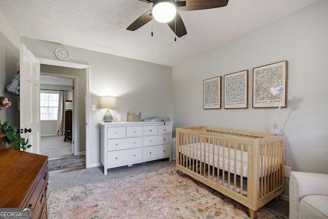 carpeted bedroom featuring a crib, ceiling fan, and a textured ceiling