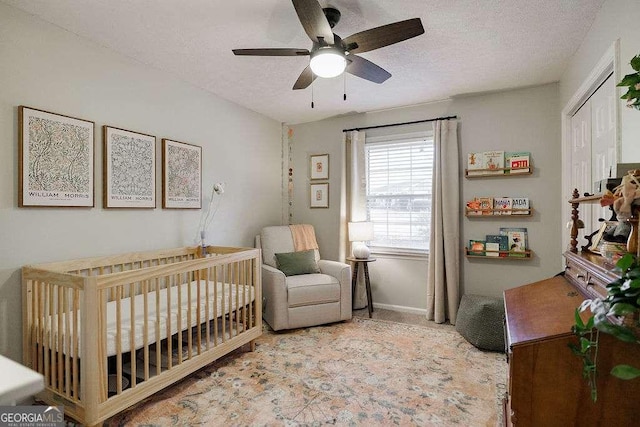 bedroom with a crib, ceiling fan, light colored carpet, and a textured ceiling