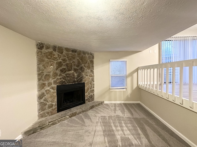 unfurnished living room featuring a stone fireplace, carpet flooring, a textured ceiling, and plenty of natural light