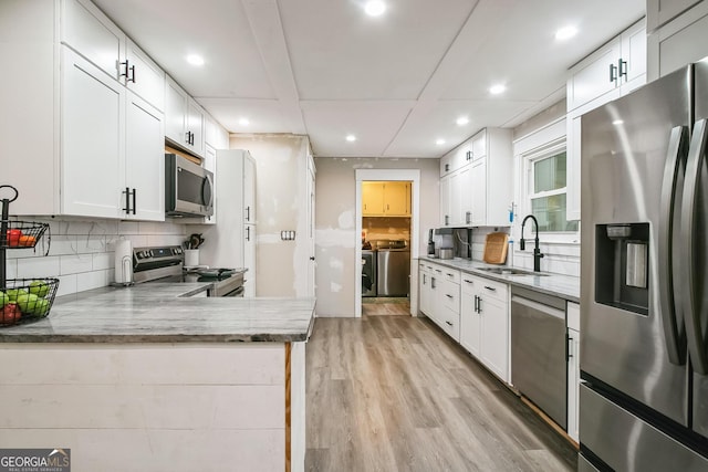 kitchen featuring sink, washer and clothes dryer, appliances with stainless steel finishes, white cabinetry, and kitchen peninsula