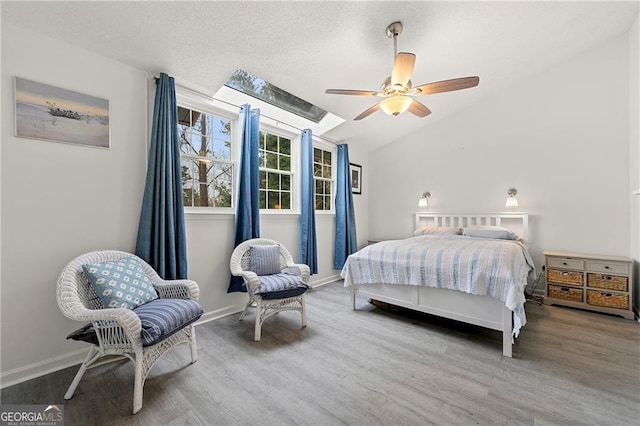 bedroom featuring ceiling fan, lofted ceiling with skylight, hardwood / wood-style floors, and a textured ceiling