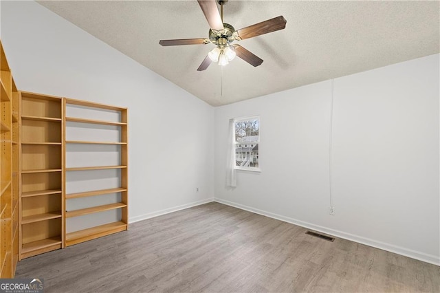 empty room featuring ceiling fan, lofted ceiling, hardwood / wood-style floors, and a textured ceiling