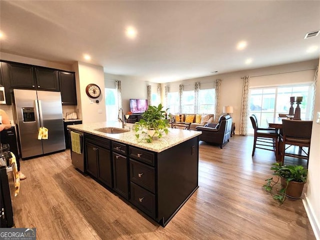 kitchen with an island with sink, sink, stainless steel appliances, light stone countertops, and light wood-type flooring