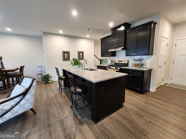 kitchen with dark wood-type flooring, a breakfast bar, sink, gas range, and a kitchen island with sink