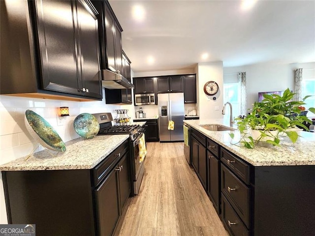 kitchen with sink, stainless steel appliances, light hardwood / wood-style floors, light stone countertops, and decorative backsplash