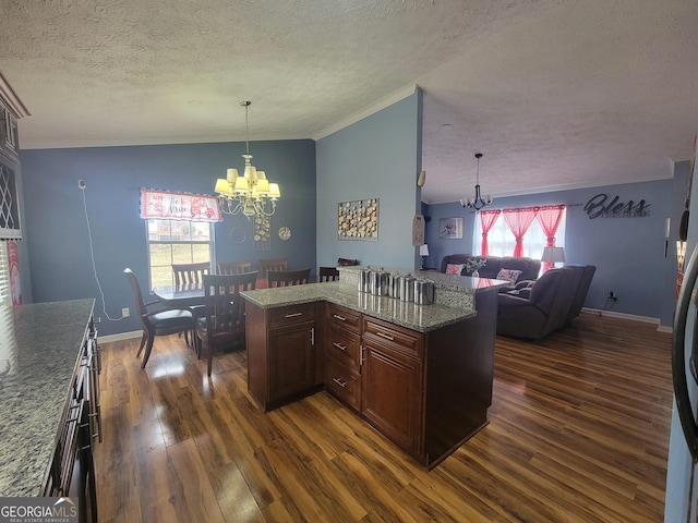 kitchen featuring hanging light fixtures, dark wood-type flooring, a textured ceiling, a notable chandelier, and open floor plan