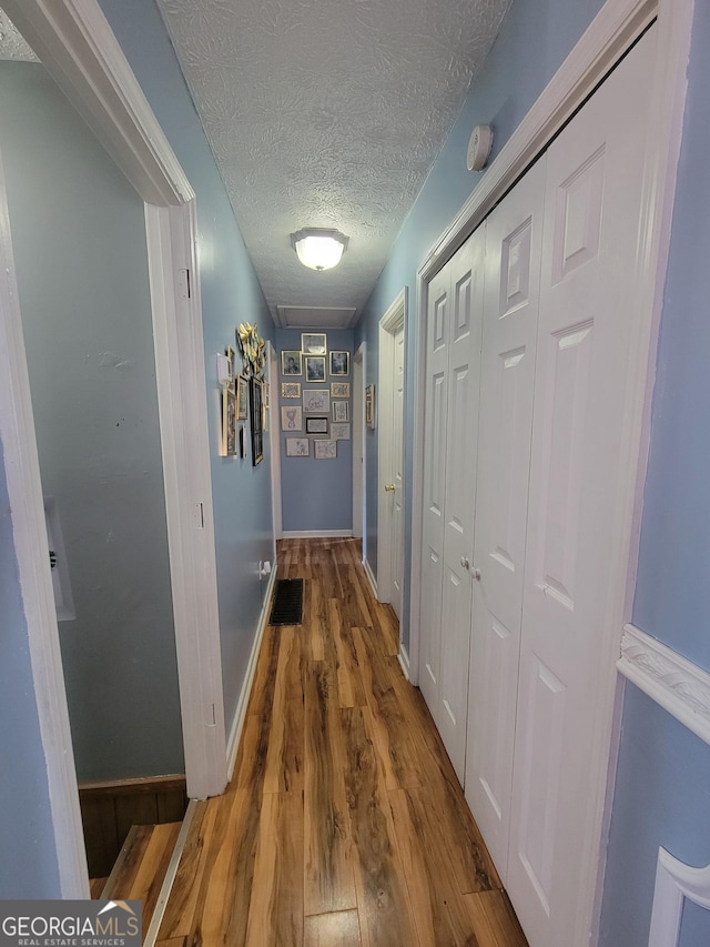 hallway featuring wood finished floors, baseboards, and a textured ceiling