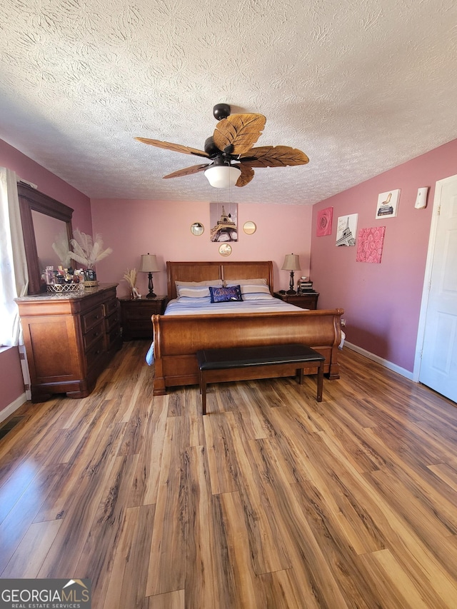 bedroom featuring ceiling fan, a textured ceiling, baseboards, and wood finished floors