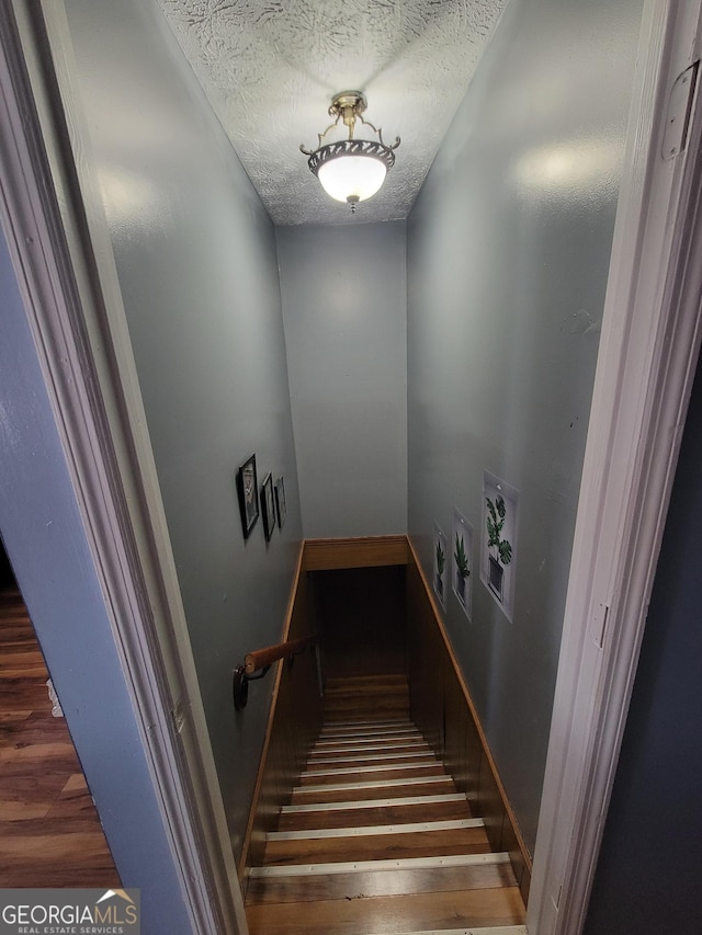 stairway with a textured ceiling and wood finished floors