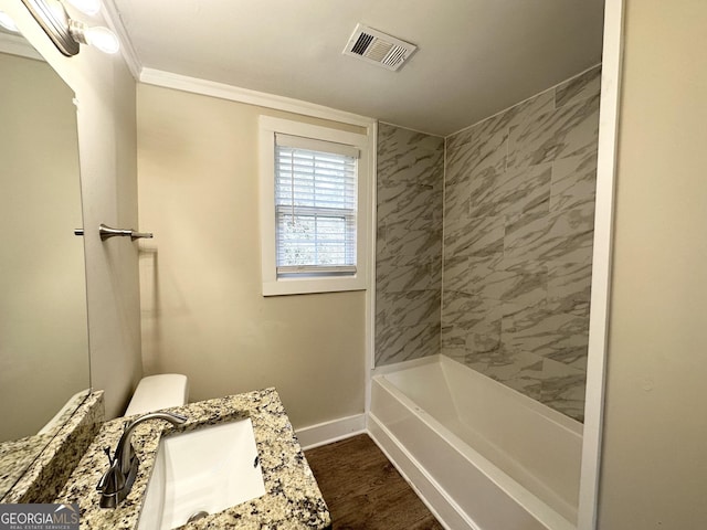 full bathroom with tiled shower / bath, hardwood / wood-style flooring, vanity, ornamental molding, and toilet