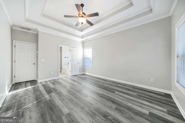 unfurnished bedroom featuring connected bathroom, crown molding, dark hardwood / wood-style floors, a raised ceiling, and ceiling fan