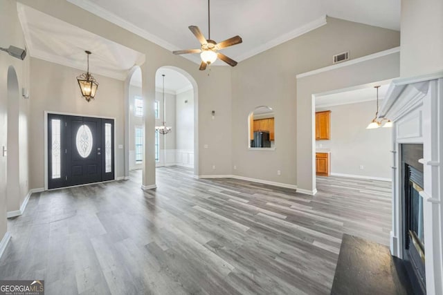 entryway featuring crown molding, hardwood / wood-style floors, a towering ceiling, and ceiling fan with notable chandelier