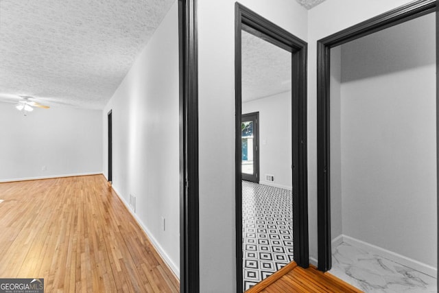 hallway featuring visible vents, a textured ceiling, and baseboards