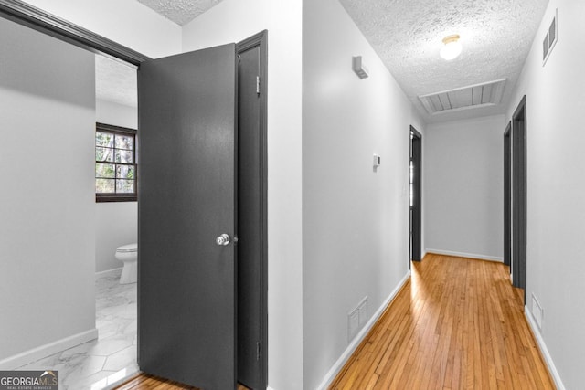 corridor with a textured ceiling and light hardwood / wood-style flooring