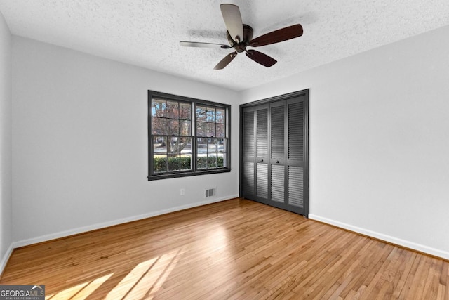 unfurnished bedroom with ceiling fan, a textured ceiling, a closet, and light wood-type flooring