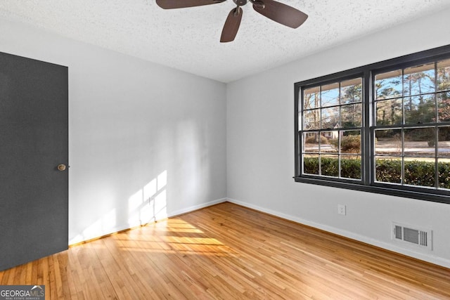 unfurnished room with a textured ceiling, a ceiling fan, baseboards, wood finished floors, and visible vents