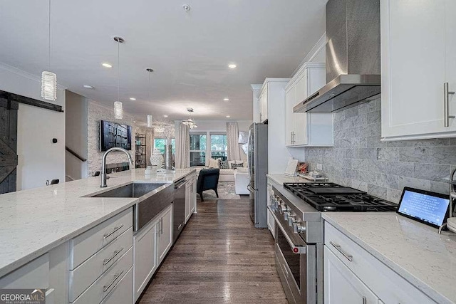 kitchen featuring appliances with stainless steel finishes, white cabinetry, sink, hanging light fixtures, and wall chimney exhaust hood