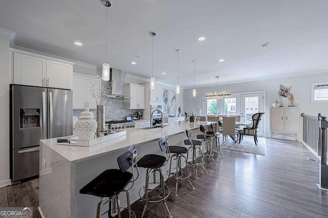 kitchen featuring white cabinetry, stainless steel fridge with ice dispenser, pendant lighting, a large island, and wall chimney range hood