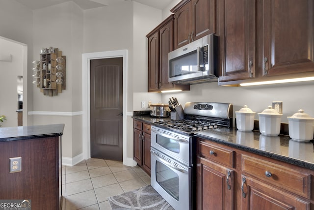 kitchen featuring dark brown cabinetry, light tile patterned floors, dark stone counters, and appliances with stainless steel finishes