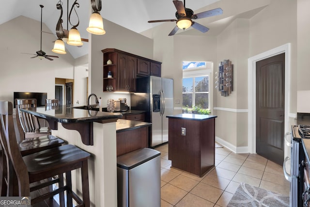 kitchen featuring dark brown cabinetry, a breakfast bar area, a center island, light tile patterned floors, and stainless steel appliances