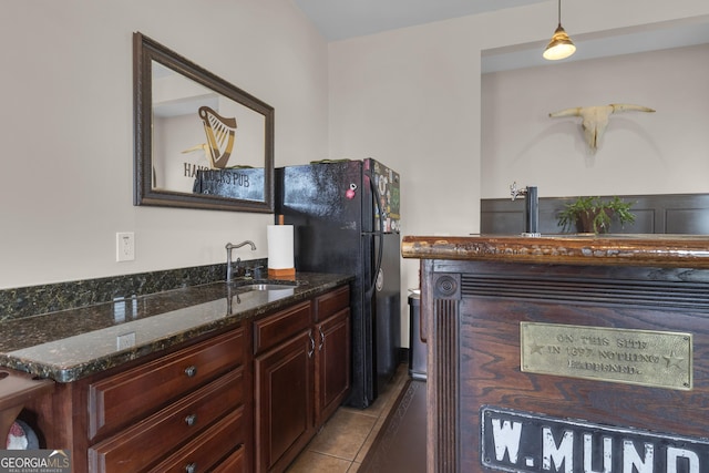 kitchen with sink, light tile patterned floors, dark stone countertops, black fridge, and decorative light fixtures