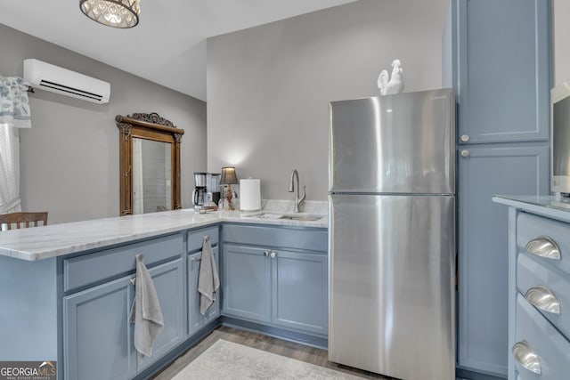 kitchen with sink, light stone counters, an AC wall unit, stainless steel refrigerator, and kitchen peninsula